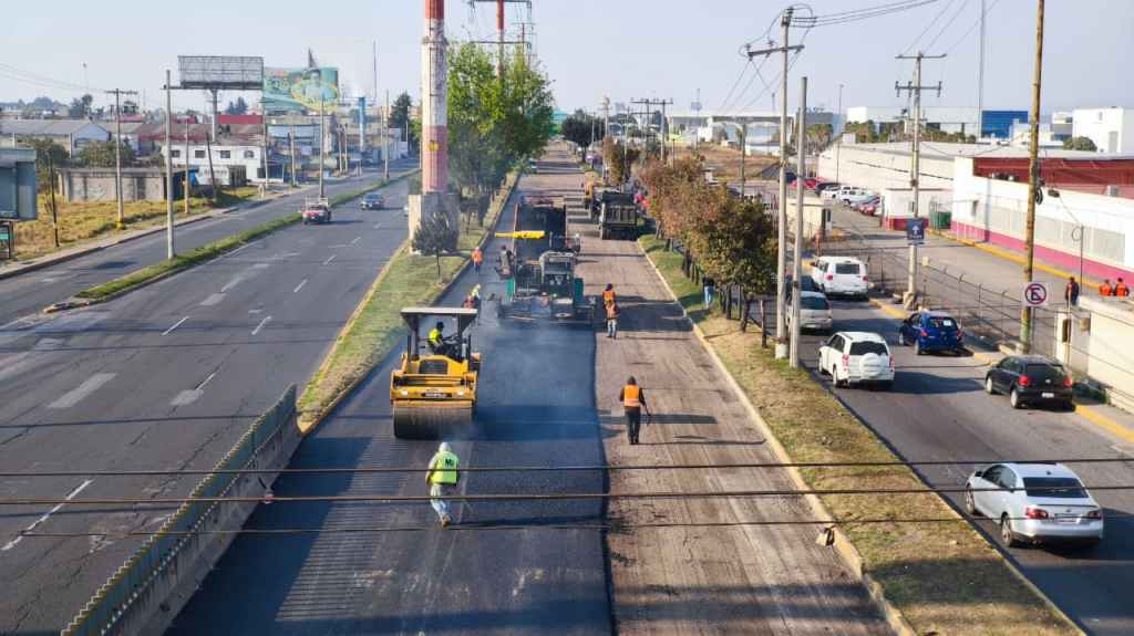 Construction workers applying asphalt on a busy road with heavy machinery and vehicles nearby.
