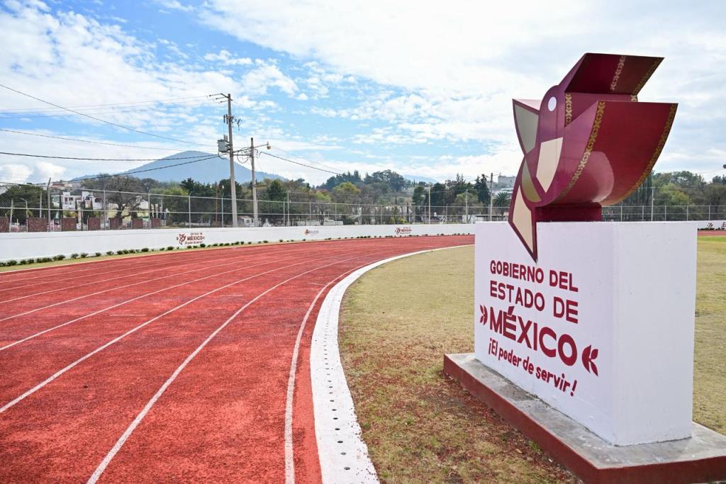 A red athletic track with a mountainscape in the background, featuring a monument that reads 'Gobierno del Estado de México' and the phrase '¡El poder de servir!'