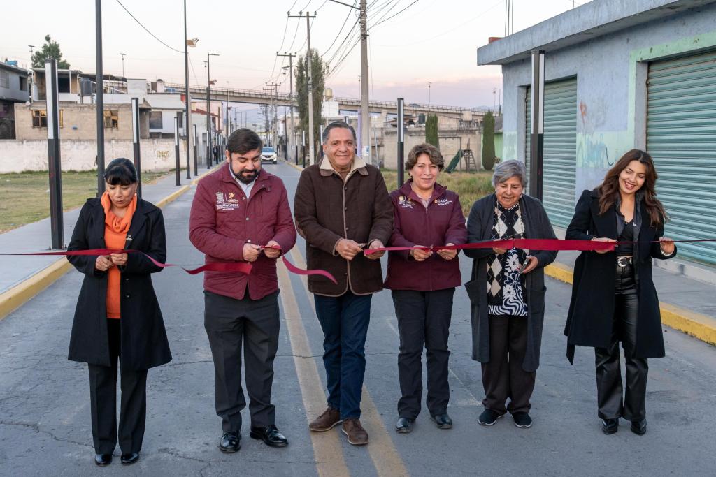 A group of six individuals standing in a street, participating in a ribbon-cutting ceremony. They are dressed in formal attire and are holding a large red ribbon, poised to cut it. In the background, there are buildings and a clear sky, indicating an urban setting.