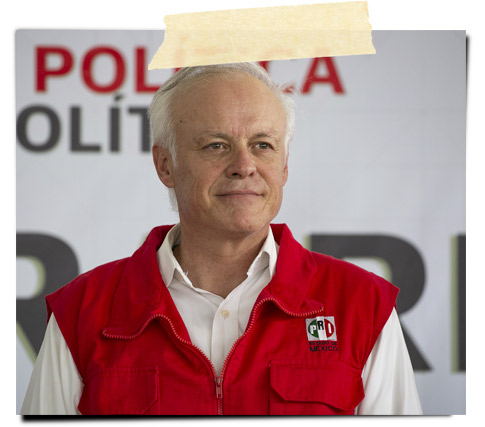 Un hombre de cabello corto y canoso, viste un chaleco rojo con el emblema del PRD. Está de pie, sonriendo levemente frente a un fondo con el logotipo del partido.