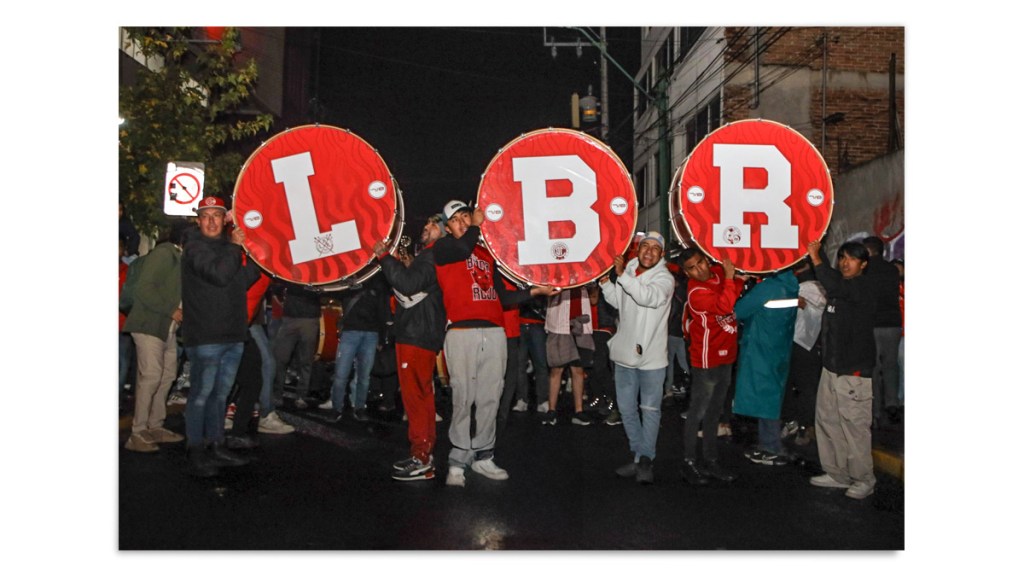 Grupo de aficionados sosteniendo tambores grandes con las letras 'I', 'B' y 'R' en una celebración, rodeados de otros seguidores en un ambiente nocturno.