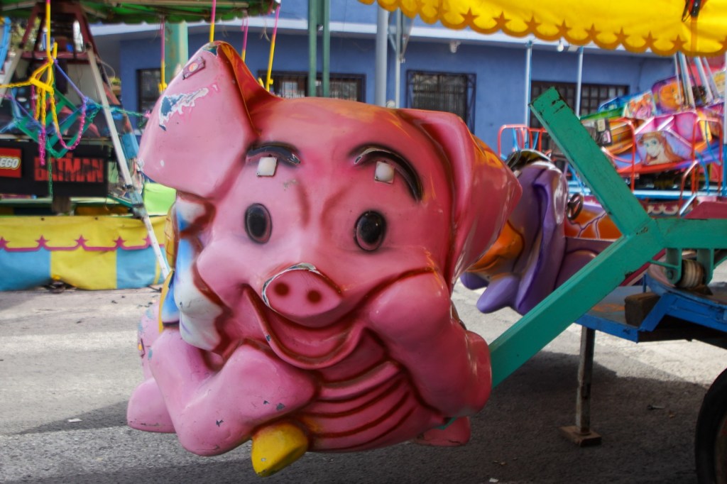 A colorful, smiling pink pig character from a carnival ride, displayed prominently with a playful expression.