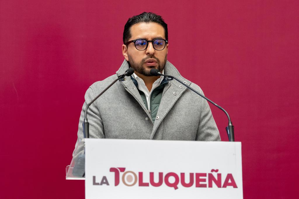 Un funcionario habla en una conferencia de prensa sobre el Programa Hoy No Circula en Toluca frente a un fondo rojo con el logotipo de La Tolqueña.