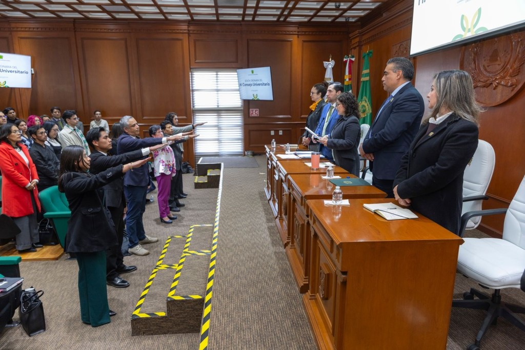 A group of people standing with raised right hands in an official setting, participating in a ceremony, with a panel of officials seated at a table in front of them.