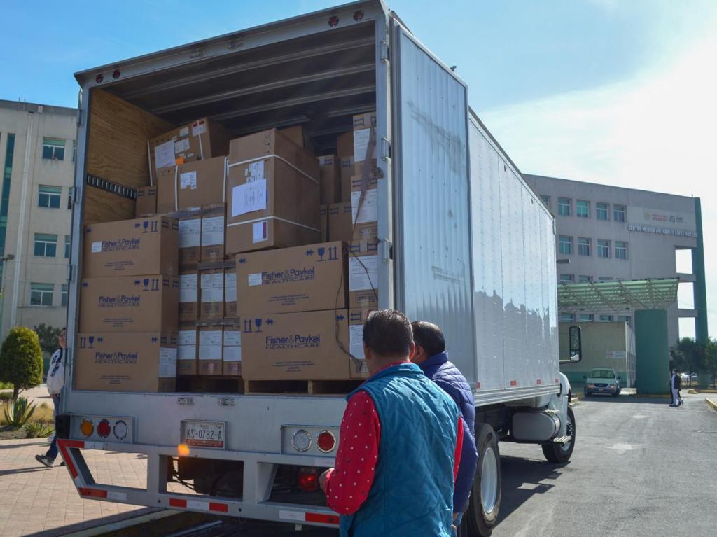 A delivery truck filled with cardboard boxes labeled Fisher & Paykel, with two people observing the load in front of a building.