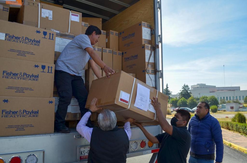 Four individuals unloading boxes from a delivery truck, with stacked cartons labeled Fisher & Paykel Healthcare in the background.