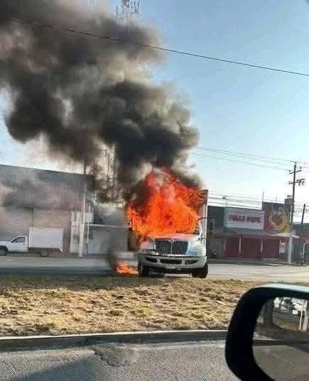 Camión en llamas emitiendo humo negro en la carretera.