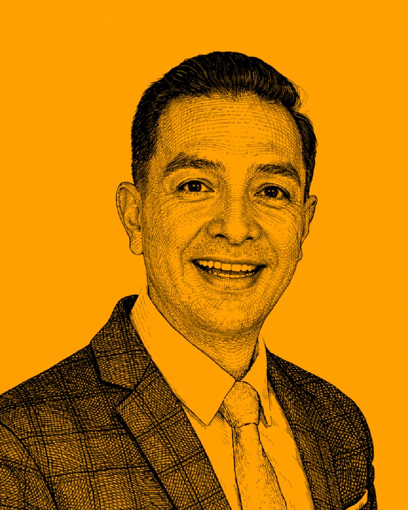 Retrato de un hombre sonriendo, vestido con traje de cuadros y corbata, sobre un fondo naranja.