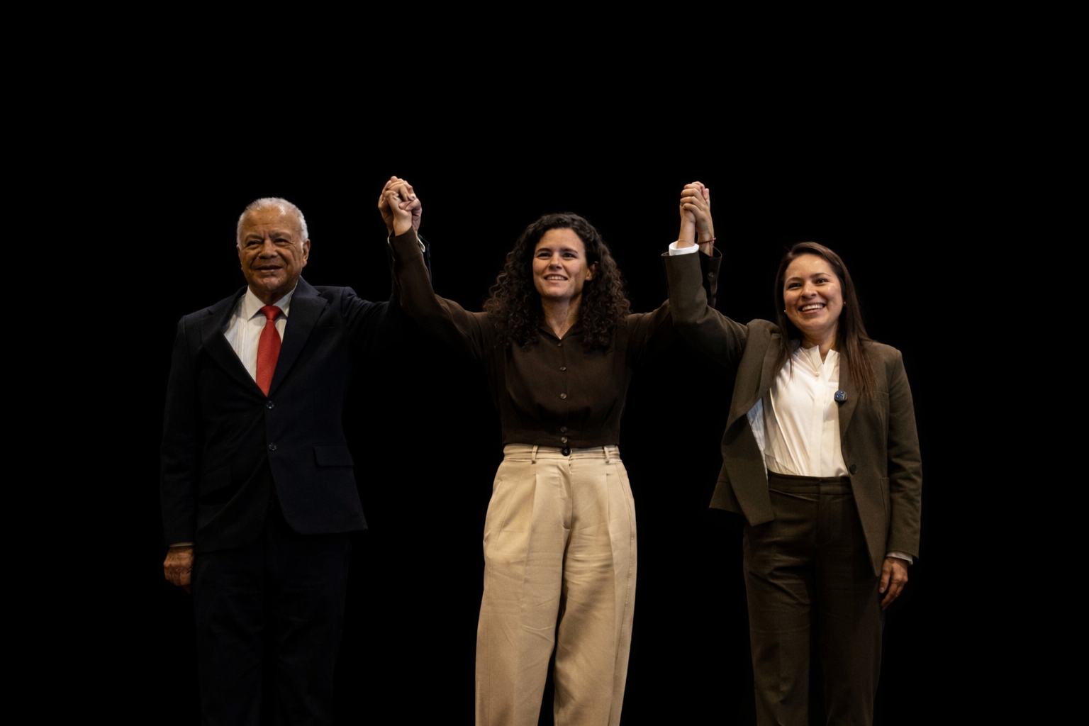 Representantes de Morena, PT y PVEM levantando las manos en señal de unidad sobre fondo negro durante evento rumbo al 2027.