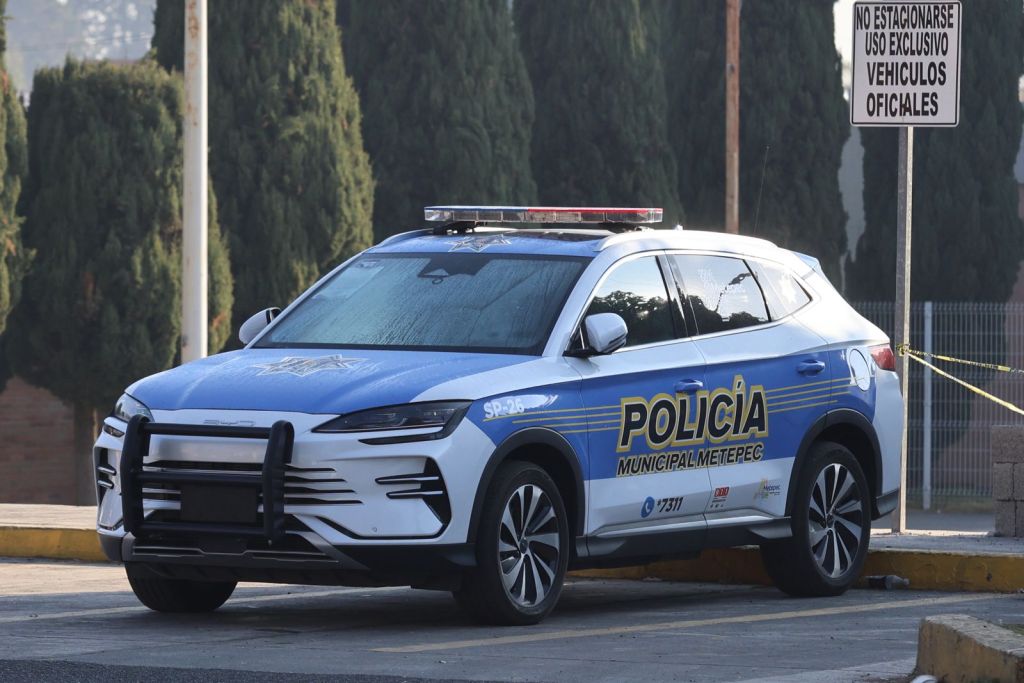 A municipal police vehicle parked, displaying the words 'Policía Municipal Metepec' on its side, with a blue and white design and emergency lights on top.