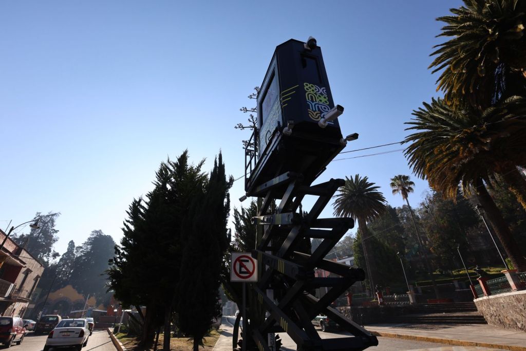 A raised platform scissor lift displaying a colorful advertisement, surrounded by palm trees and a clear blue sky.