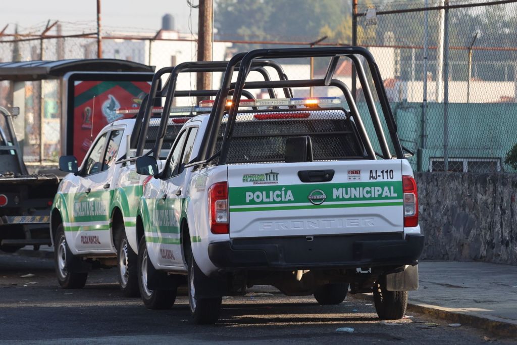 Two municipal police pickup trucks parked side by side, featuring green and white markings and safety equipment on the roof.