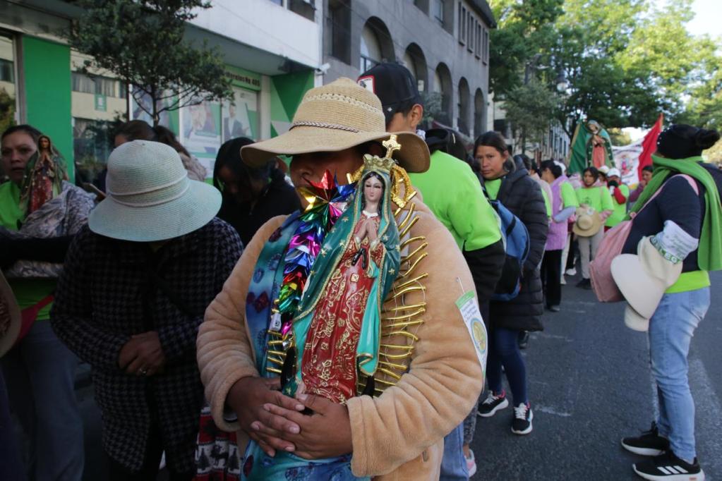 Mujer en una manifestación sosteniendo una figura de la Virgen, rodeada de otras personas con camisetas verdes y sombreros.