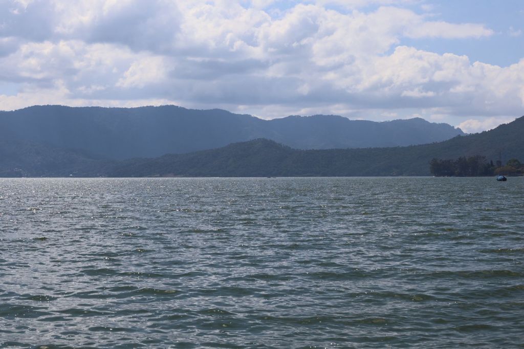 Vista panorámica de un lago rodeado de montañas y nubes en el cielo.