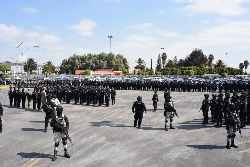Formación de un gran grupo de policías y personal de seguridad en un estacionamiento, equipados con uniformes y armas.