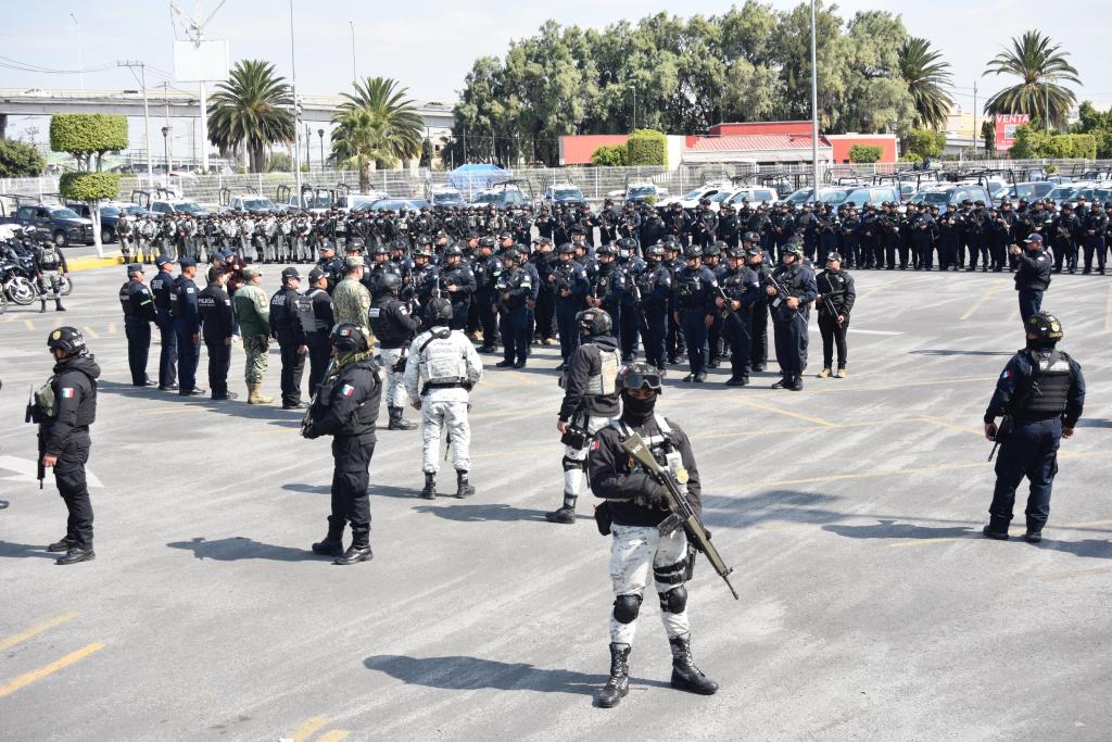 A large group of police and military personnel gathered in a parking lot for a formation. Some officers are dressed in tactical gear, while others are in uniforms. Palm trees and vehicles are visible in the background.