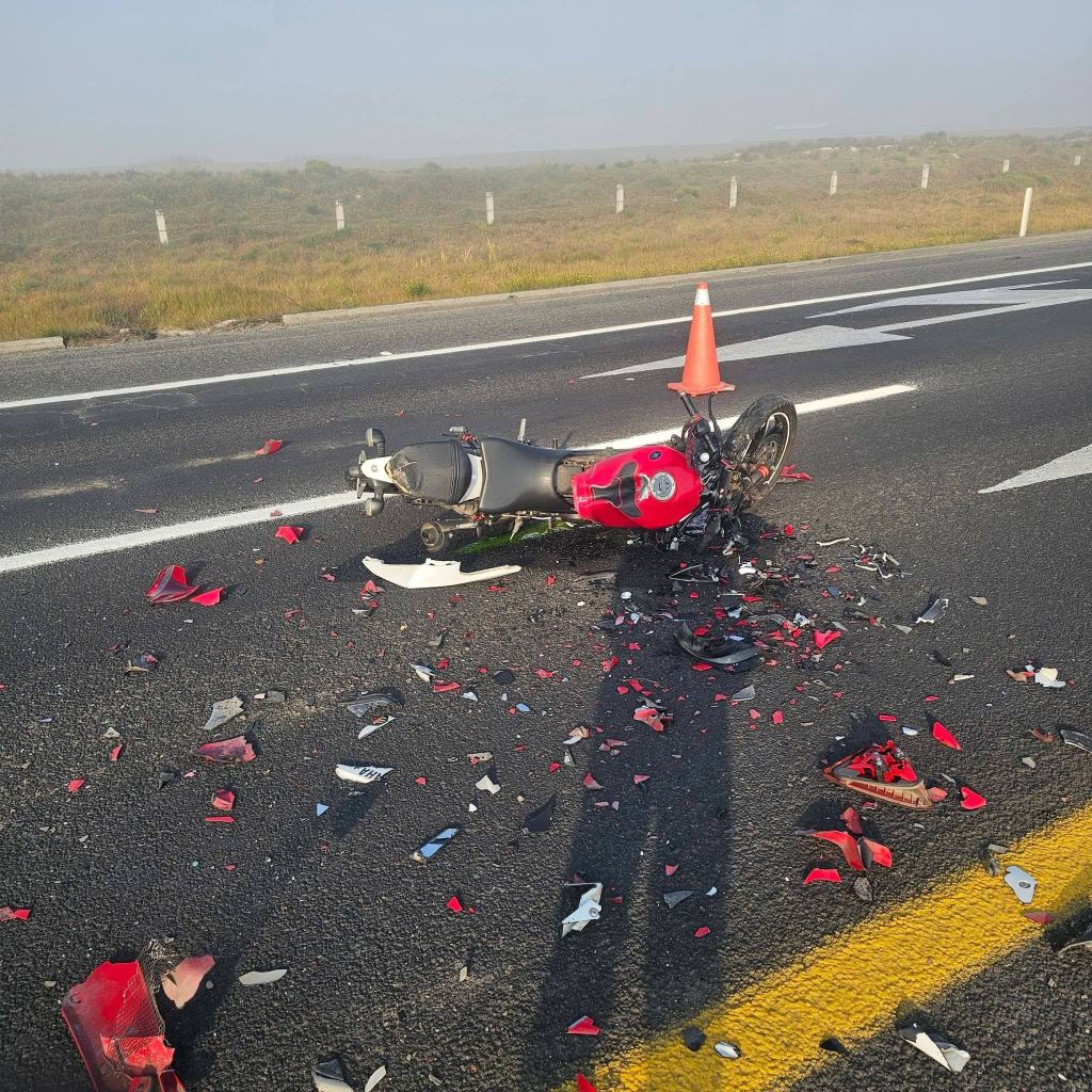 A crashed motorcycle lying on the road, surrounded by scattered debris and a traffic cone.