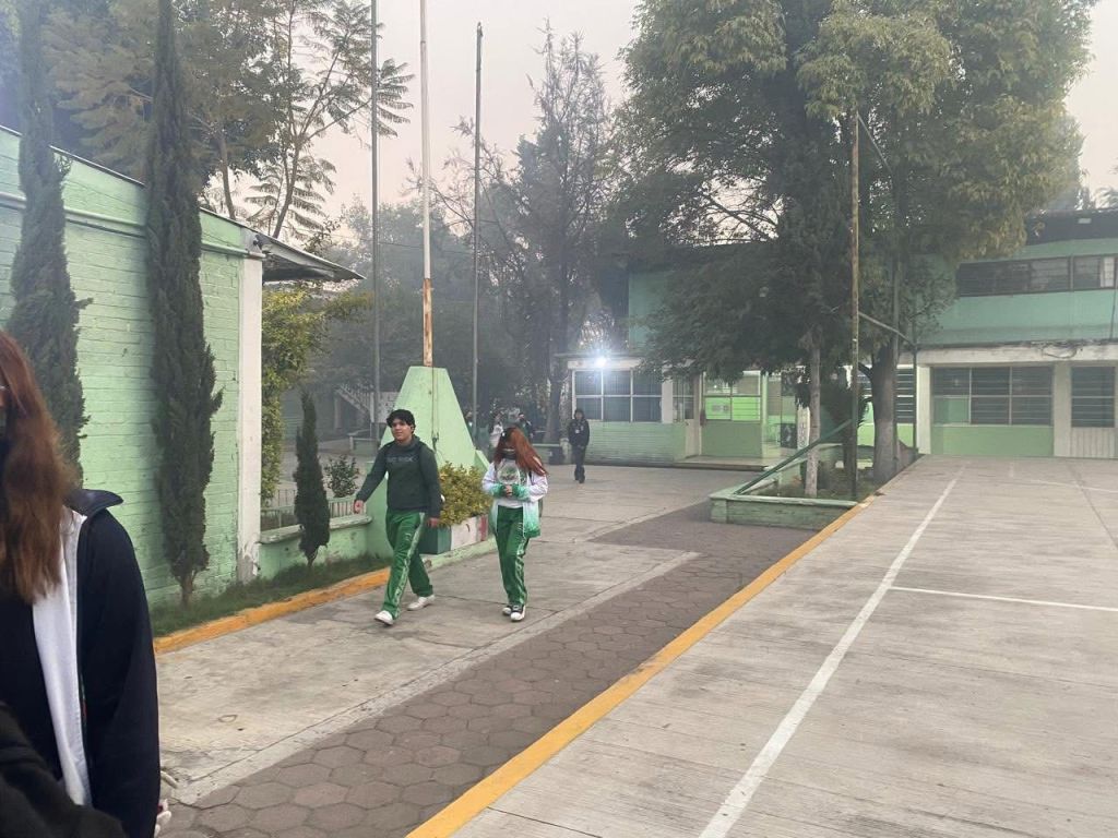 Students walking in a school courtyard surrounded by green buildings and trees, with a foggy atmosphere.