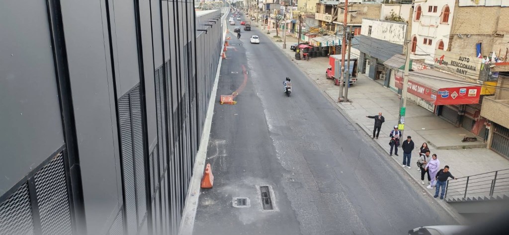 Vista de una calle con tráfico, donde se observan vehículos y personas en la acera, junto a una construcción moderna.