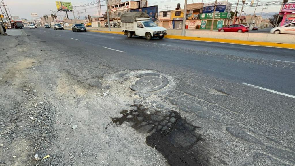 Un bache en la carretera con asfalto suelto y un círculo visible en la superficie, rodeado de tráfico de vehículos.