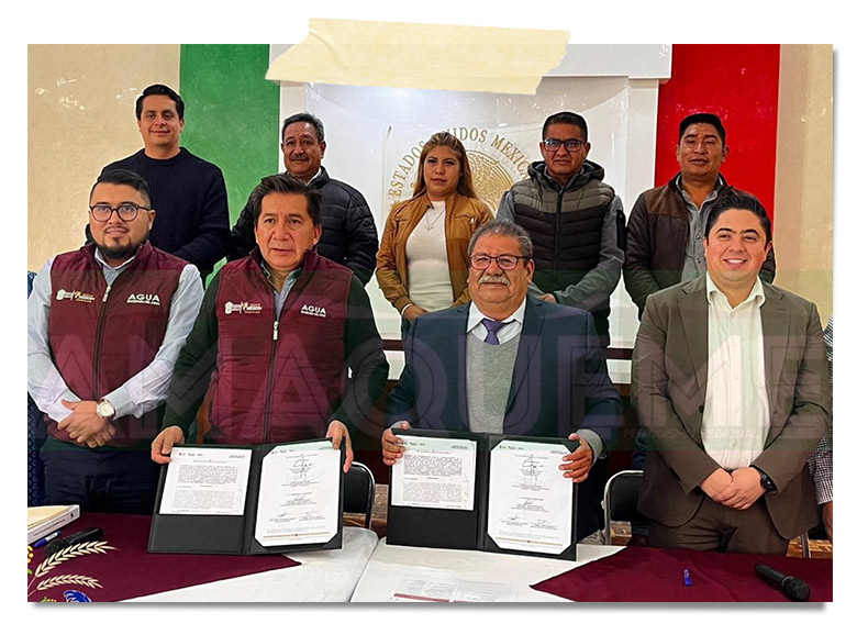 Reunión de varios funcionarios firmando documentos en una mesa, con banderas de México en el fondo.