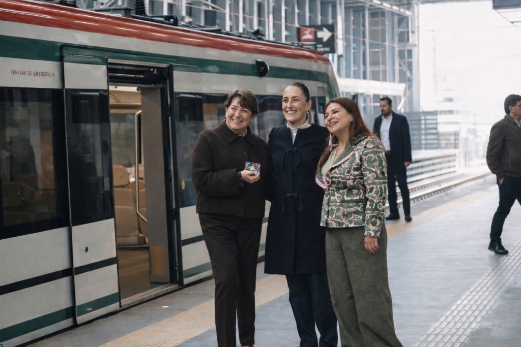 Tres mujeres posando sonrientes en una estación de tren, con un tren de fondo en la plataforma.