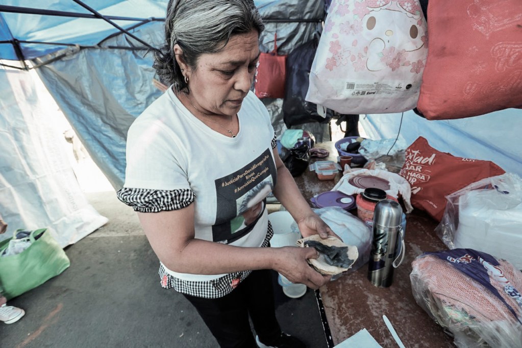 Mujer preparando comida en un puesto de mercado con una mesa llena de productos y utensilios.