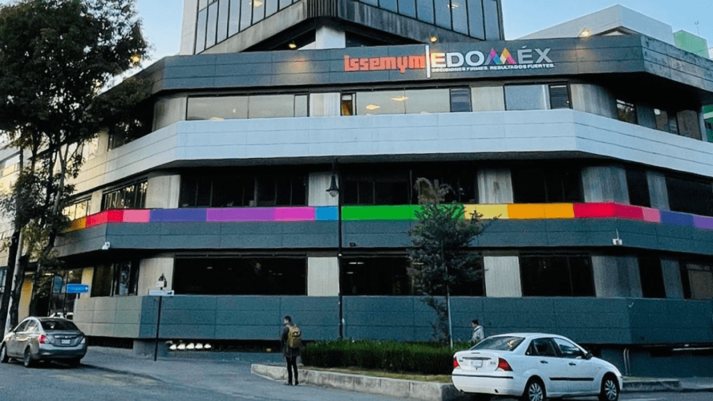 Edificio moderno con letrero que dice 'Itsemy EDOMÉX', fachada con franjas de colores y árboles en la acera.