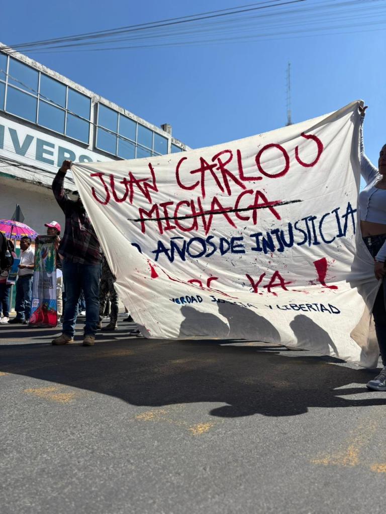 A group of protesters holding a large banner that reads 'Juan Carlos Michaca, 10 años de injusticia, ¡Justicia ya!' during a demonstration.