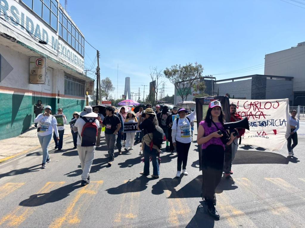 A group of people participating in a march for justice, featuring banners and signs, in front of a university building under clear skies.