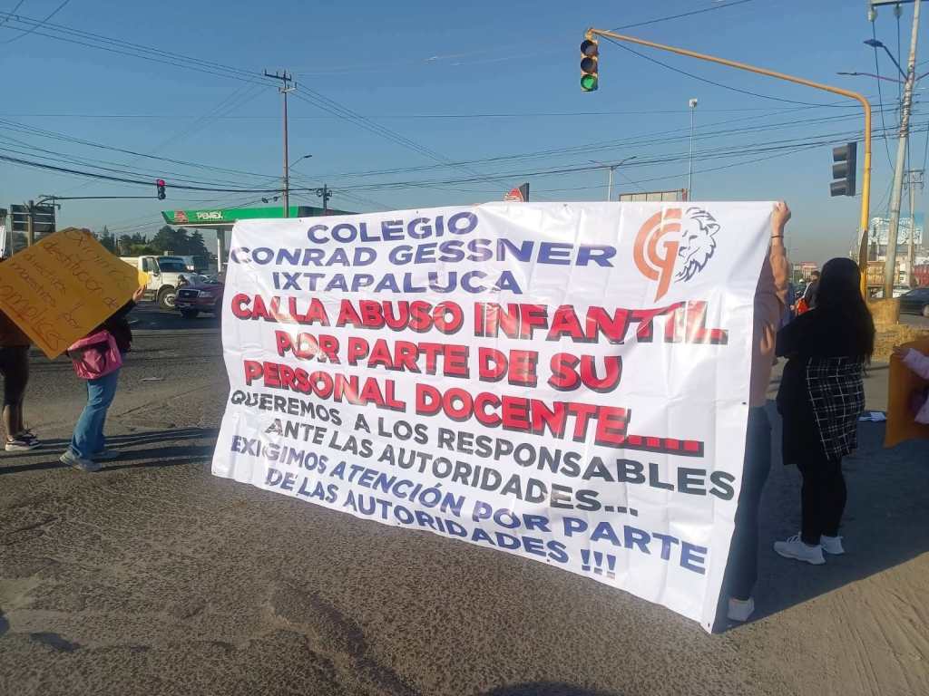 A group of protesters holding a large banner demanding attention to child abuse allegations against staff at Colegio Conrad Gessner in Ixtapaluca. The banner highlights the need for accountability from authorities.