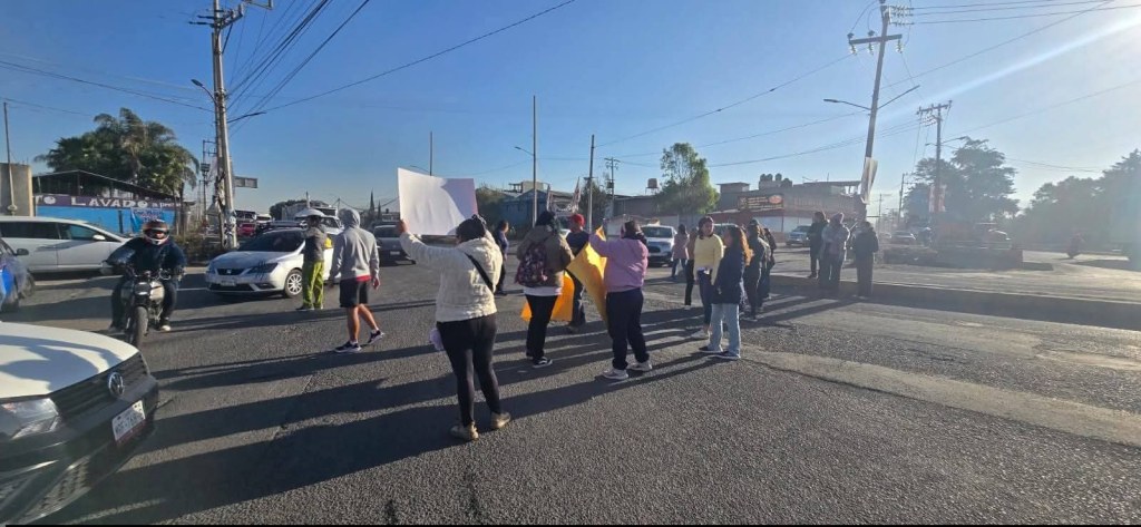 A group of protesters holding signs in the middle of a street, surrounded by cars and motorcycles during the day.