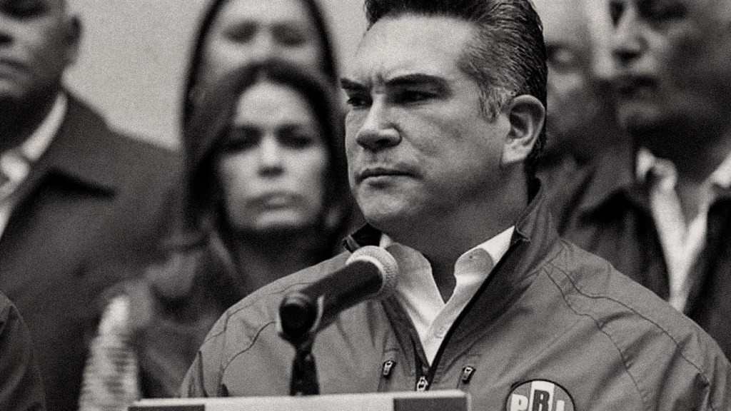Un político hablando en un micrófono durante una conferencia de prensa, con otros miembros de su partido de fondo.