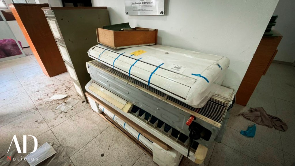 Vista de una oficina con un aire acondicionado apilado y muebles de oficina al fondo. El ambiente muestra un desorden ligero.