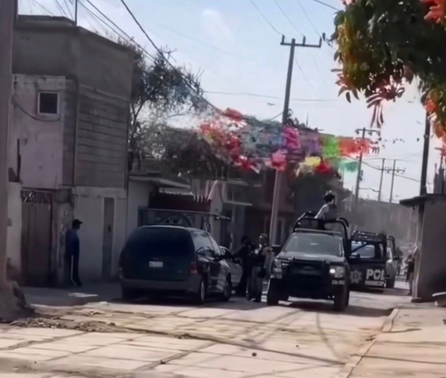 Scene of a street with police vehicles and officers, with colorful decorations overhead, indicating a festive atmosphere amidst a neighborhood.