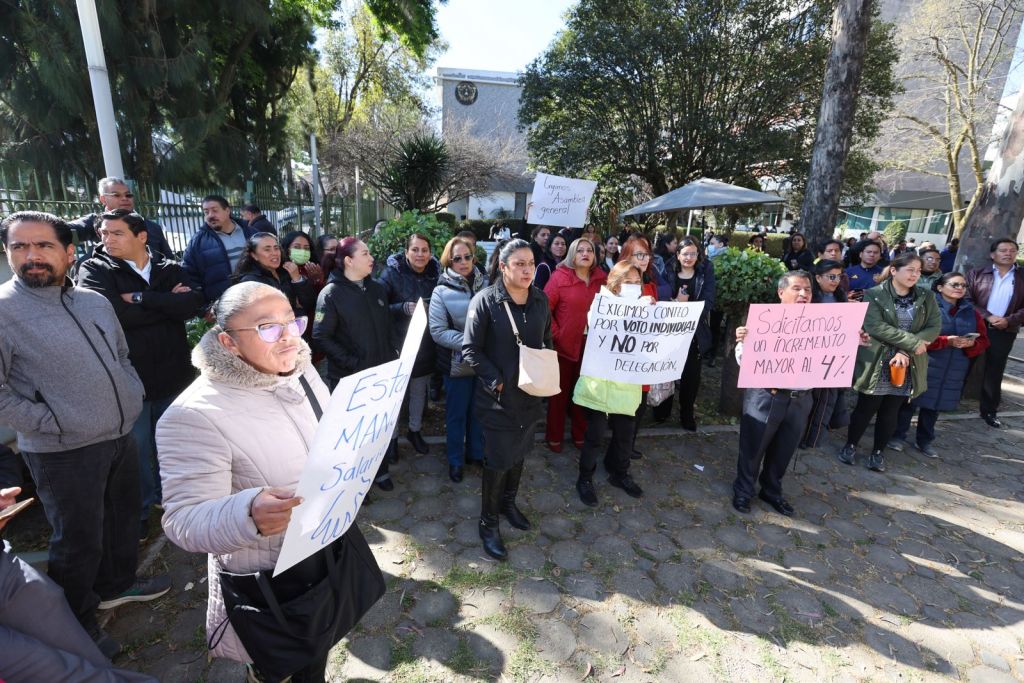 A group of protesters holding signs during a demonstration in a public area, calling for collective rights and salary increases.