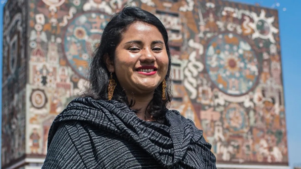 A woman smiling while wearing a black shawl with a patterned background featuring colorful murals.