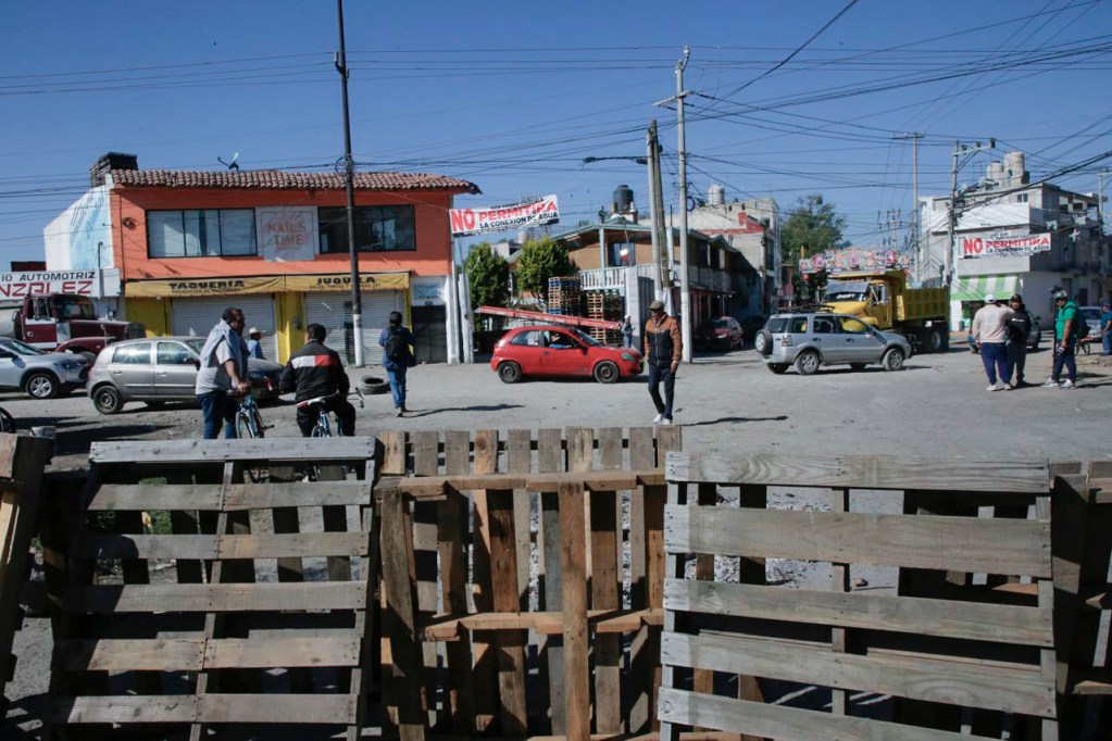 A busy intersection with multiple vehicles, bicycles, and pedestrians, featuring various businesses in the background, including a taqueria and automotive shop.