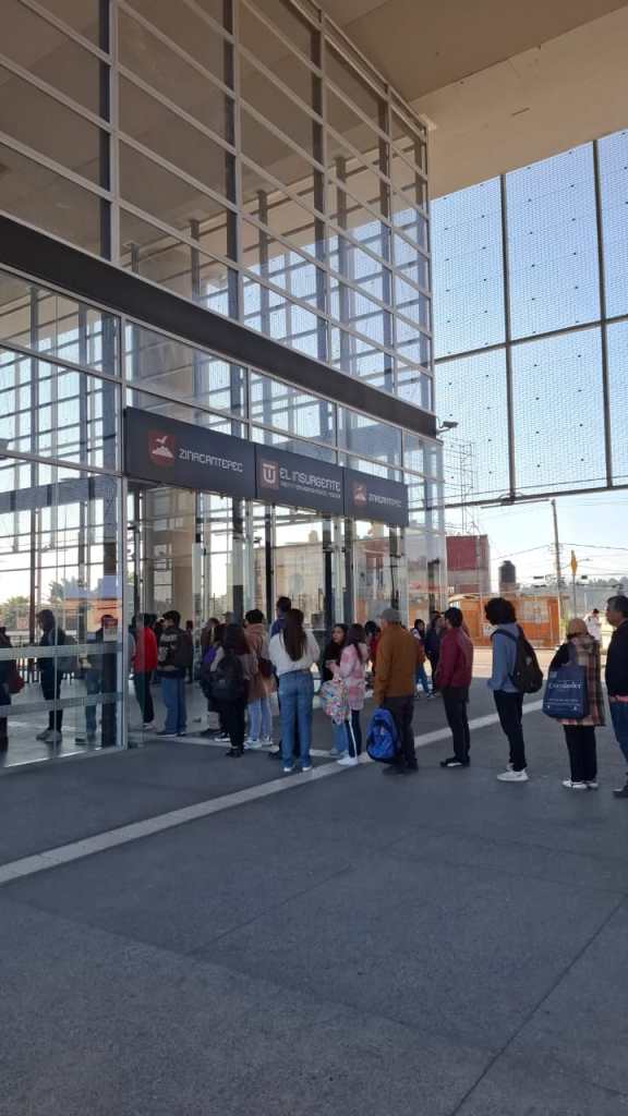 People waiting in line outside a modern glass building with signage for a public transport service.