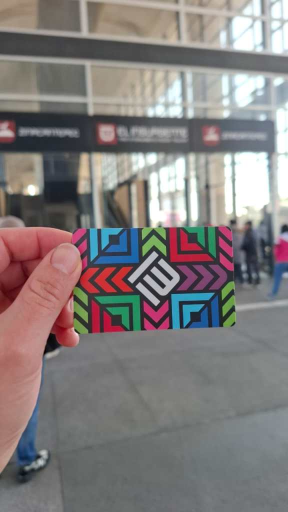 A hand holding a colorful, patterned card in front of a building entrance with large windows.