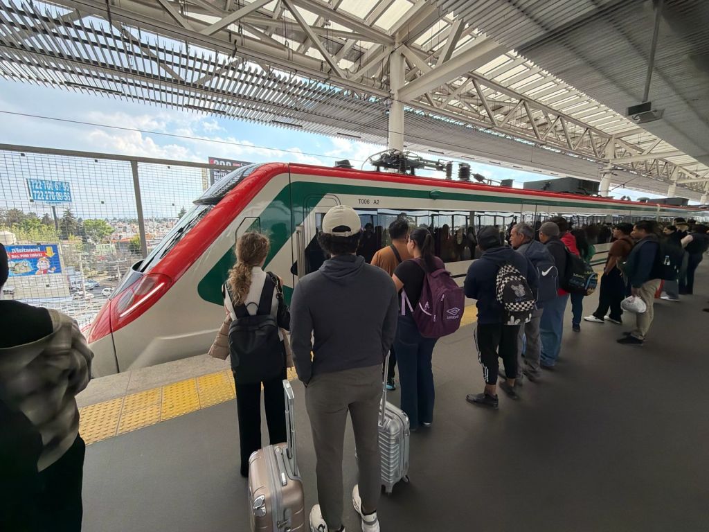 Passengers waiting at a metro station platform with a train approaching, carrying luggage and backpacks.