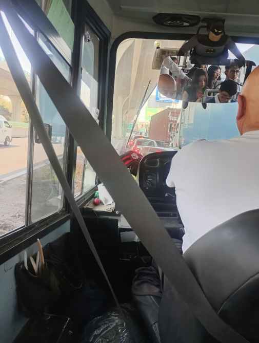 Vista del interior de un autobús, mostrando al conductor y un espejo retrovisor con reflejos de pasajeros.