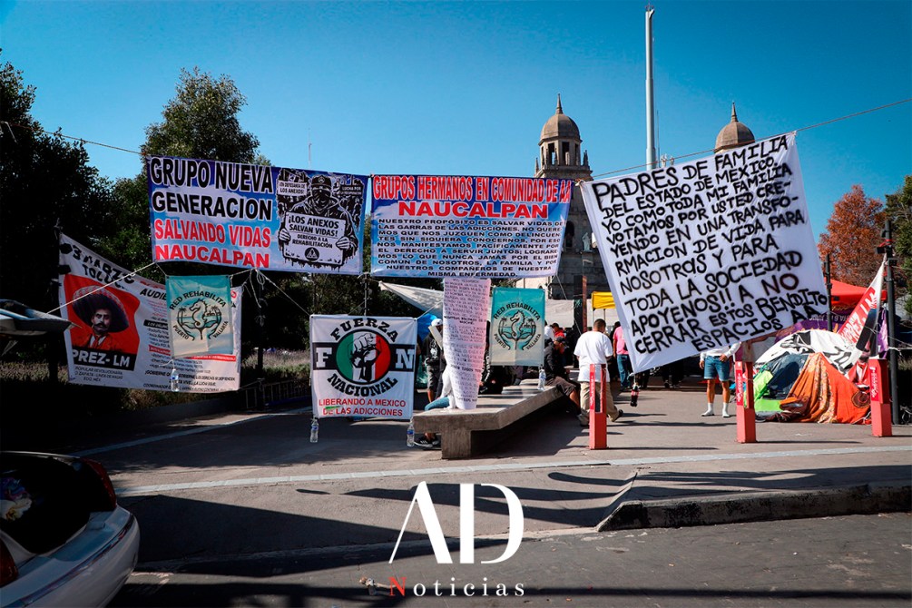 A protest scene featuring various colorful banners and signs in a public area, with messages focusing on community support and addiction recovery in Naucalpan, Mexico.