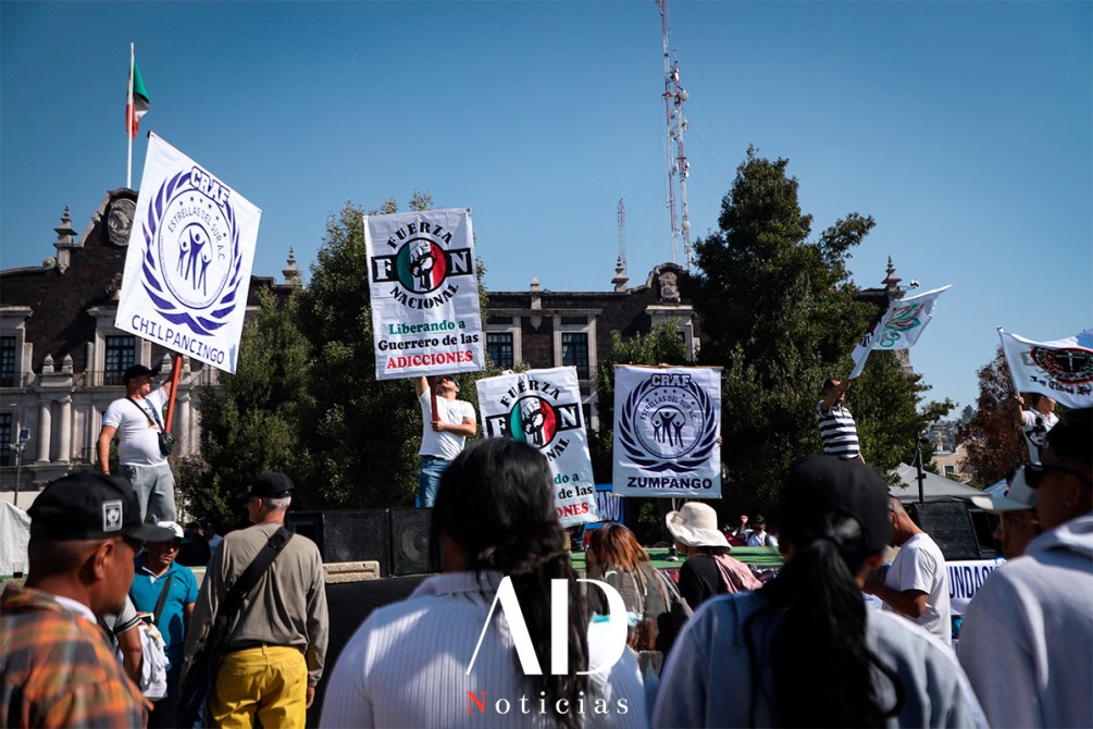 A group of protesters holding banners in a public square, advocating for addiction recovery and support, with a government building in the background.