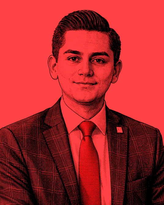 Retrato de un hombre joven con cabello oscuro, vestido con un traje de cuadros y corbata roja, contra un fondo rojo.