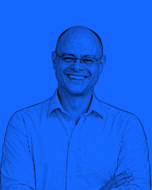 Retrato de un hombre sonriendo con fondo azul. Lleva una camiseta blanca y gafas.