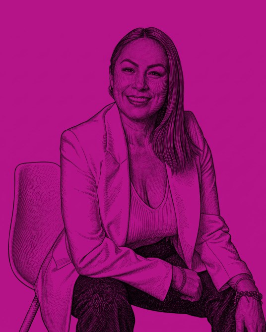 Illustrated portrait of a smiling woman with long hair, wearing a blazer, seated with one arm on her knee against a bright pink background.