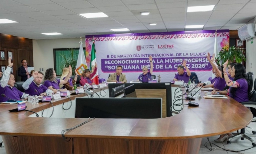 Reunión para conmemorar el Día Internacional de la Mujer en La Paz, mostrando a participantes levantando la mano en señal de aprobación.