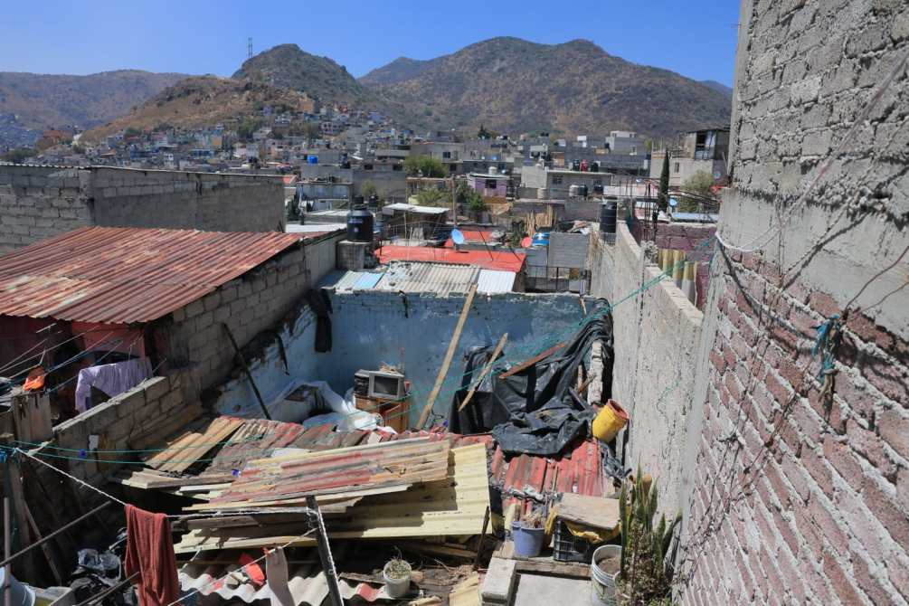 A view of a dilapidated urban area with makeshift roofs, scattered debris, and surrounding hills in the background.