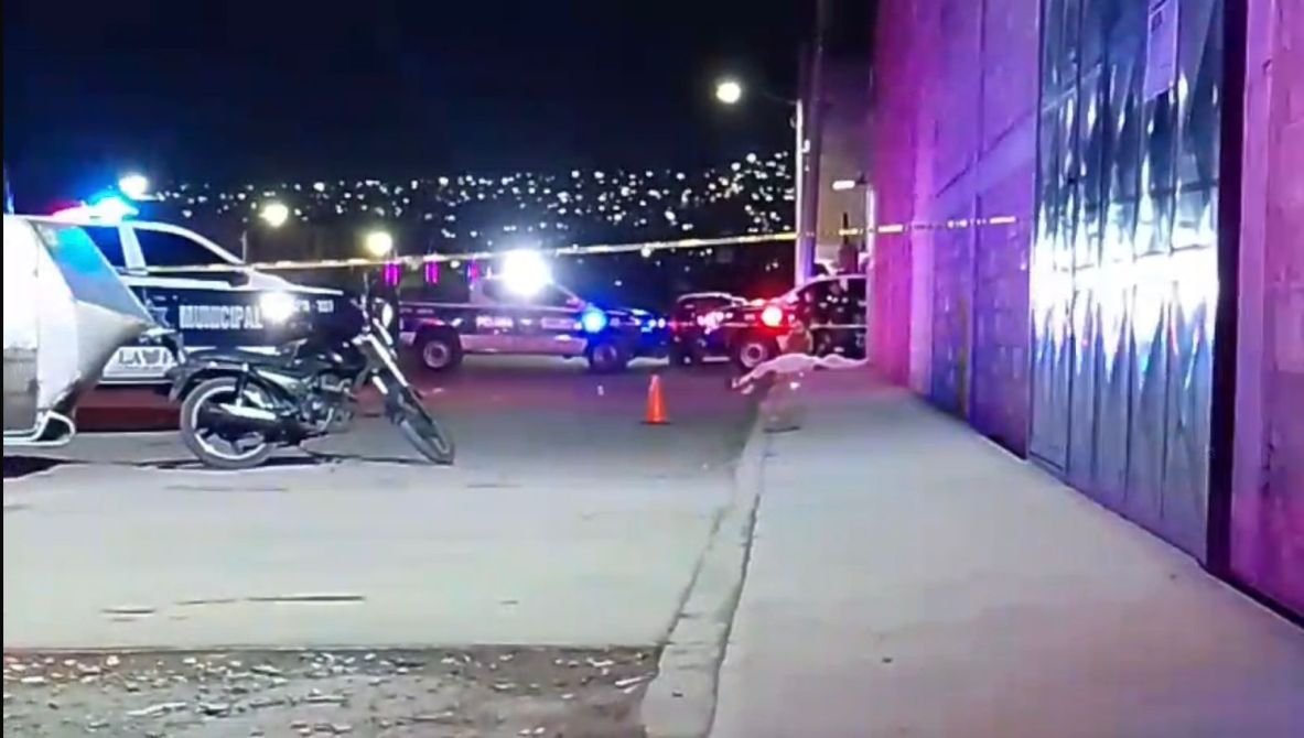 Escena del crimen con patrullas policiales y cinta de seguridad, de noche, en una calle con una motocicleta estacionada.